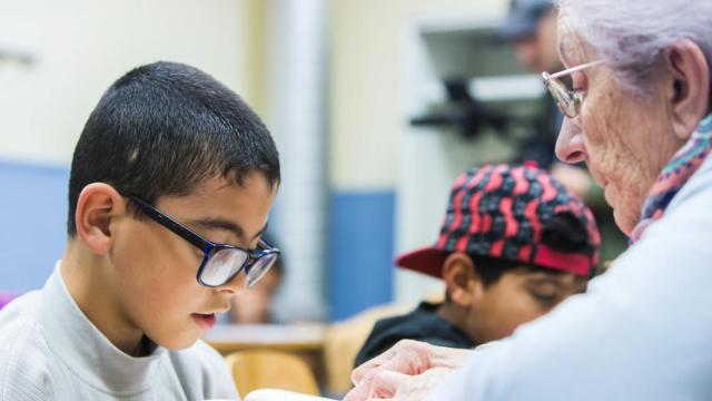 Una voluntaria mayor ayuda a un niño con sus estudios