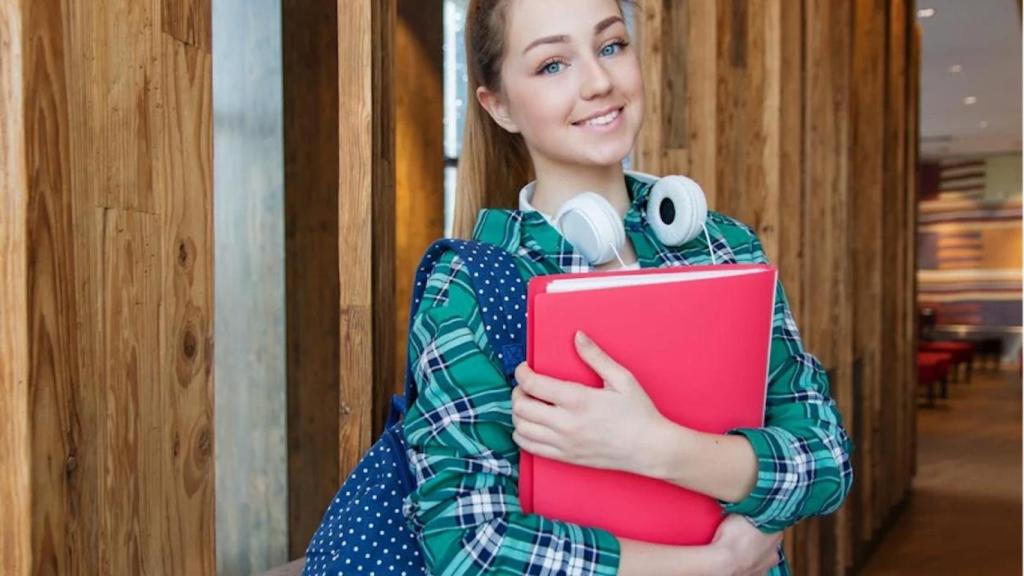 Estudiante sonríe con una carpeta sobre el pecho