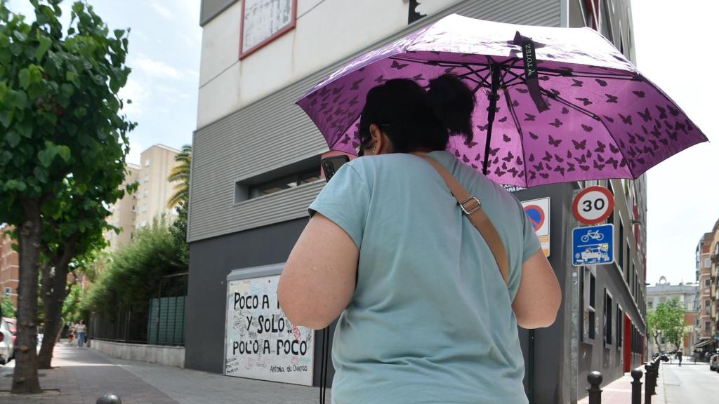 Una mujer se proteje del calor y la lluvia con un paraguas