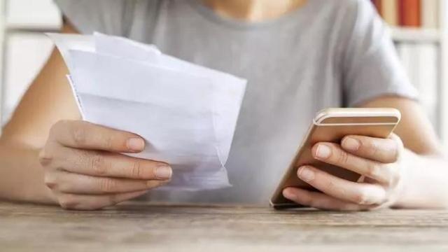 Persona sujeta un móvil y una factura