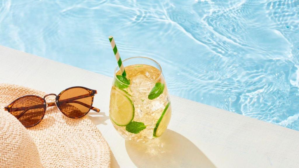 Gafas de sol, sombrero y cóctel en una piscina