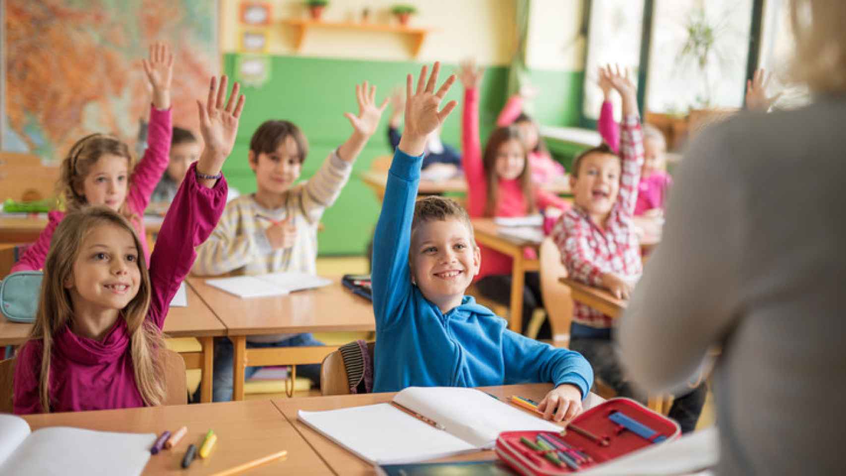 Unos alumnos levantan la mano en el clase.