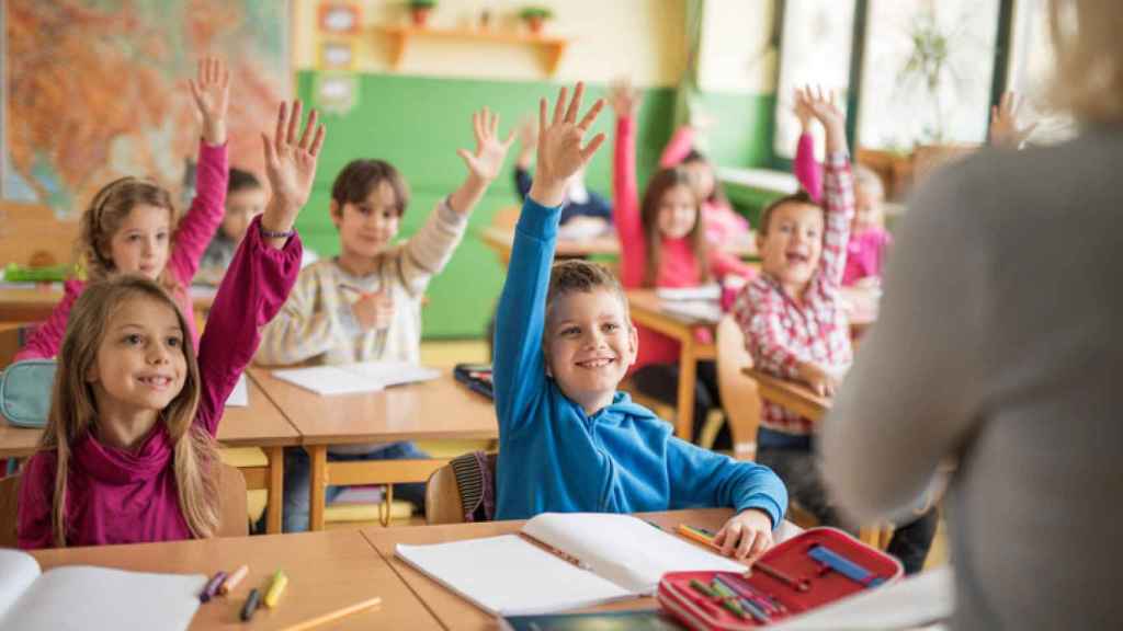 Unos alumnos levantan la mano en el clase.