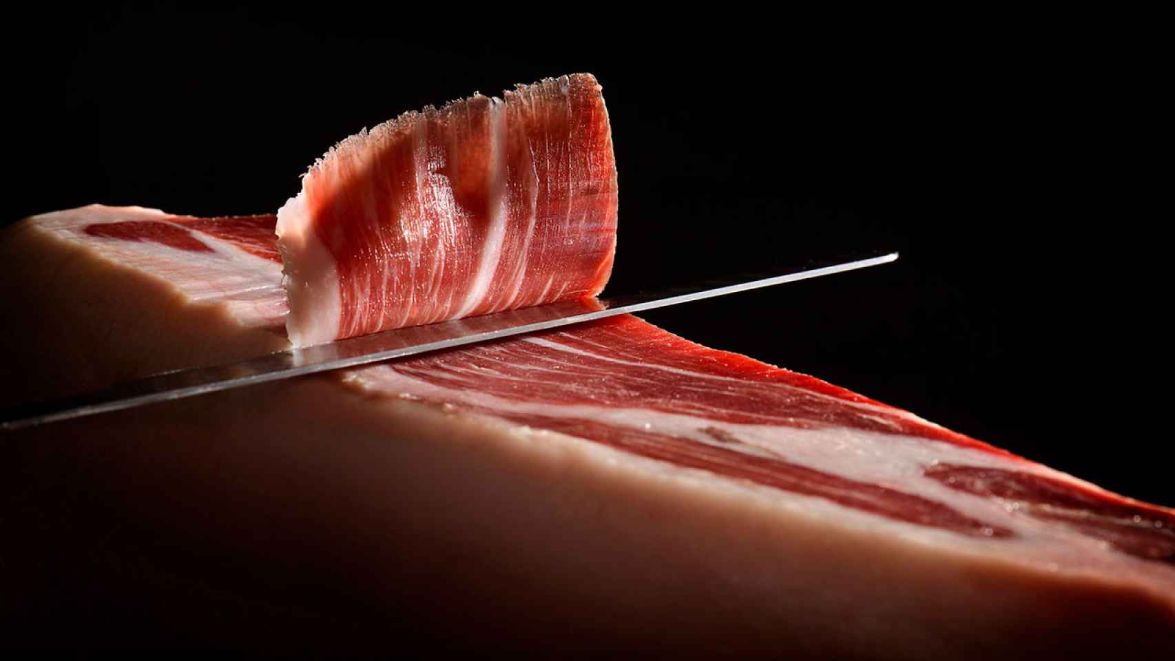 Un hombre corta una pieza de jamón serrano.