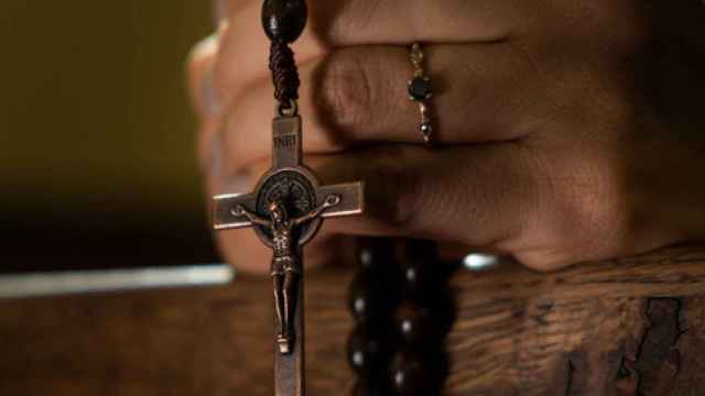 Unas manos sostienen un rosario en una iglesia.