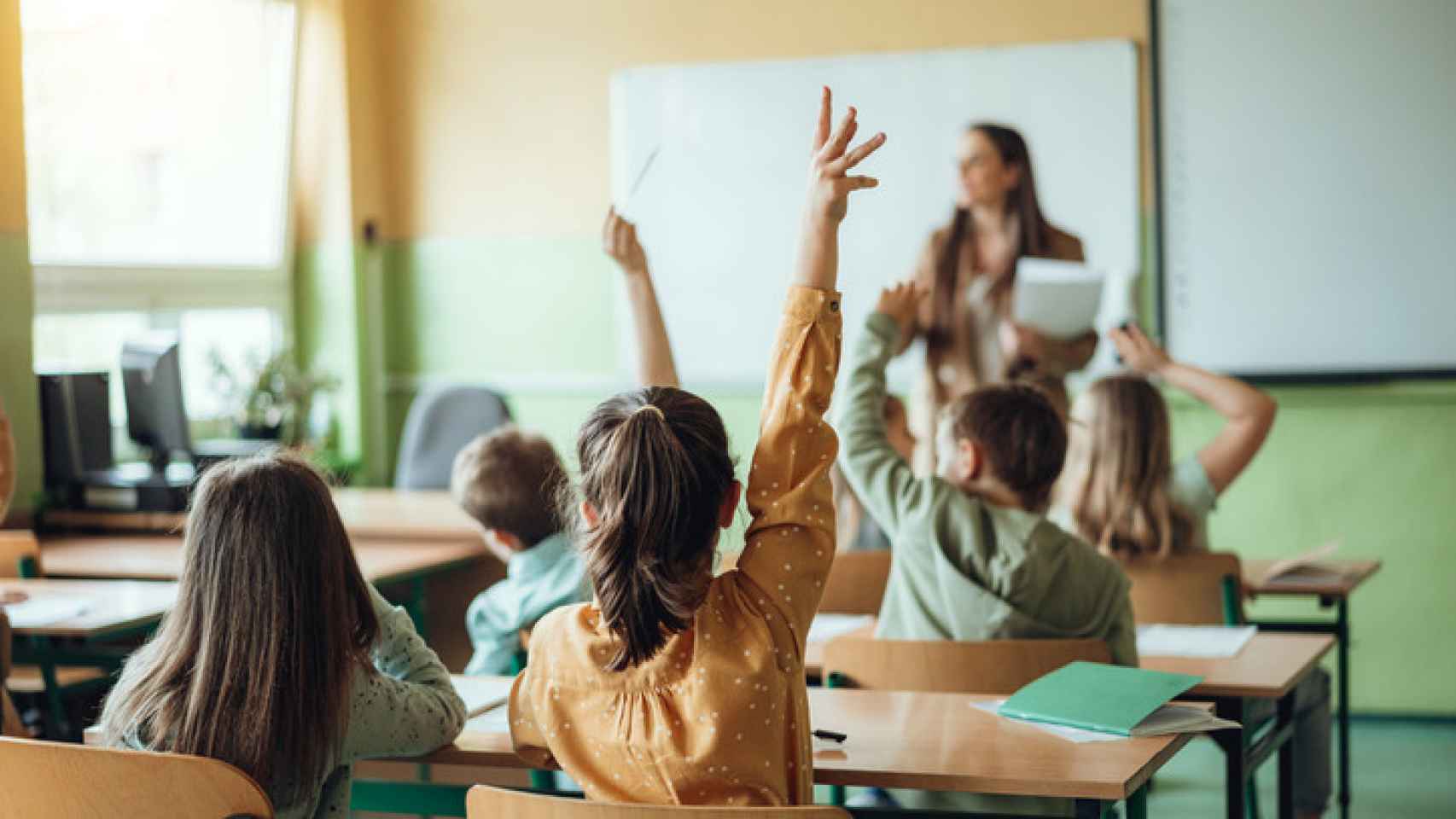 Unos alumnos atienden en clase y levantan la mano para participar.