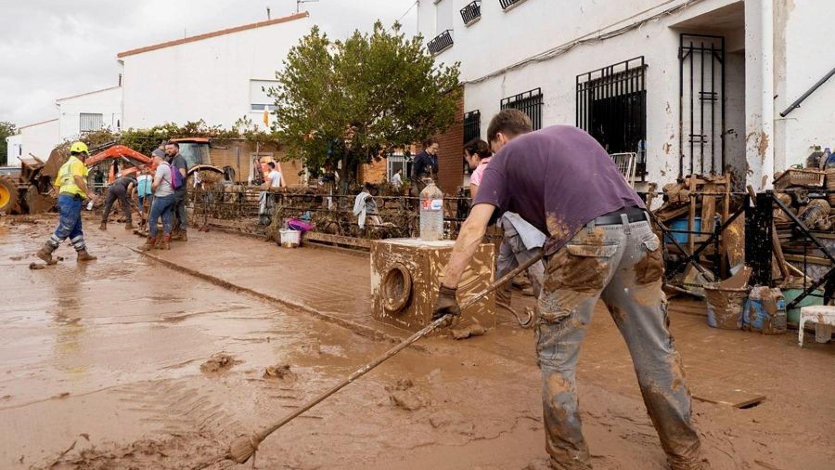 Varias personas colaboran en la limpieza de una calle tras el paso de la DANA