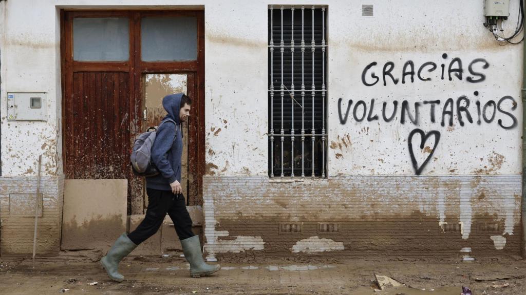 Un hombre camina junto a un graffitti que agradece la ayuda a los voluntarios mientras continúan las labores de limpieza en Paiporta