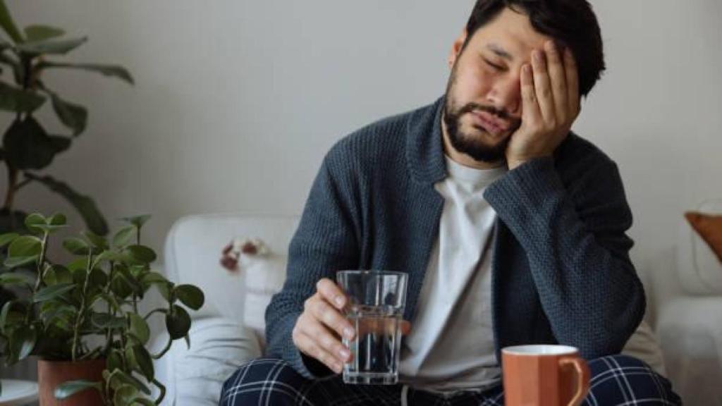 Un hombre enfrenta una resaca con dolor de cabeza.