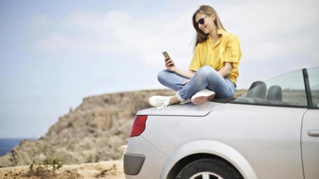 Mujer con un móvil sentada en un descapotable