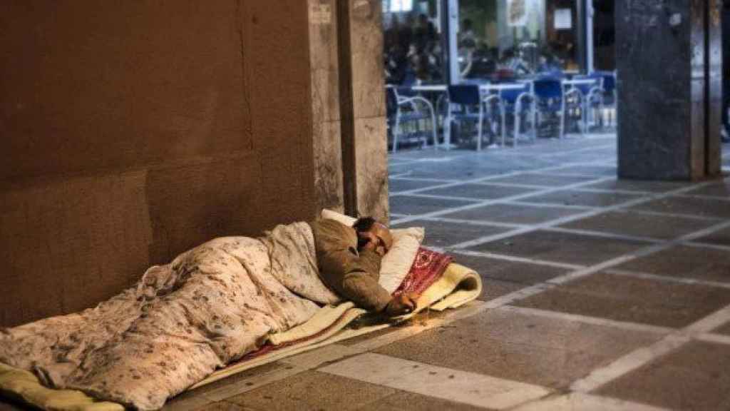 Un hombre sin techo duerme en la acera, junto a una cafetería