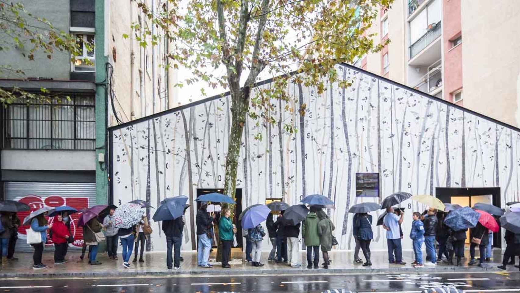 Personas haciendo cola con paraguas en Barcelona