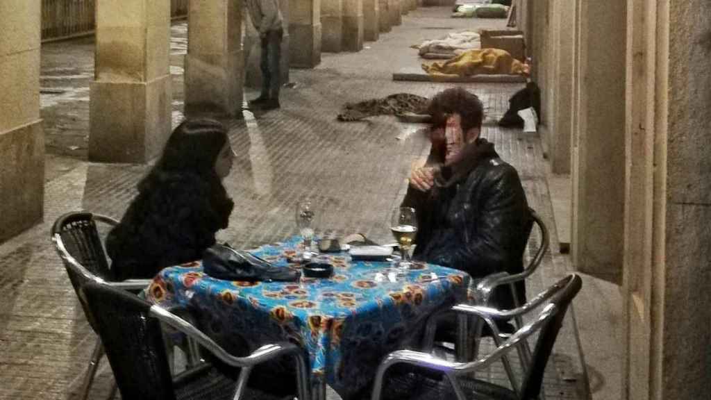 Dos personas toman algo en una  terraza mientras un sintecho orina en la calle