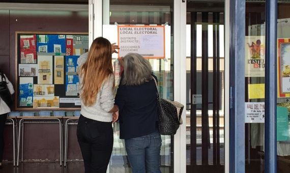 Dos apoderadas fijan el cartel de local electoral en la puerta