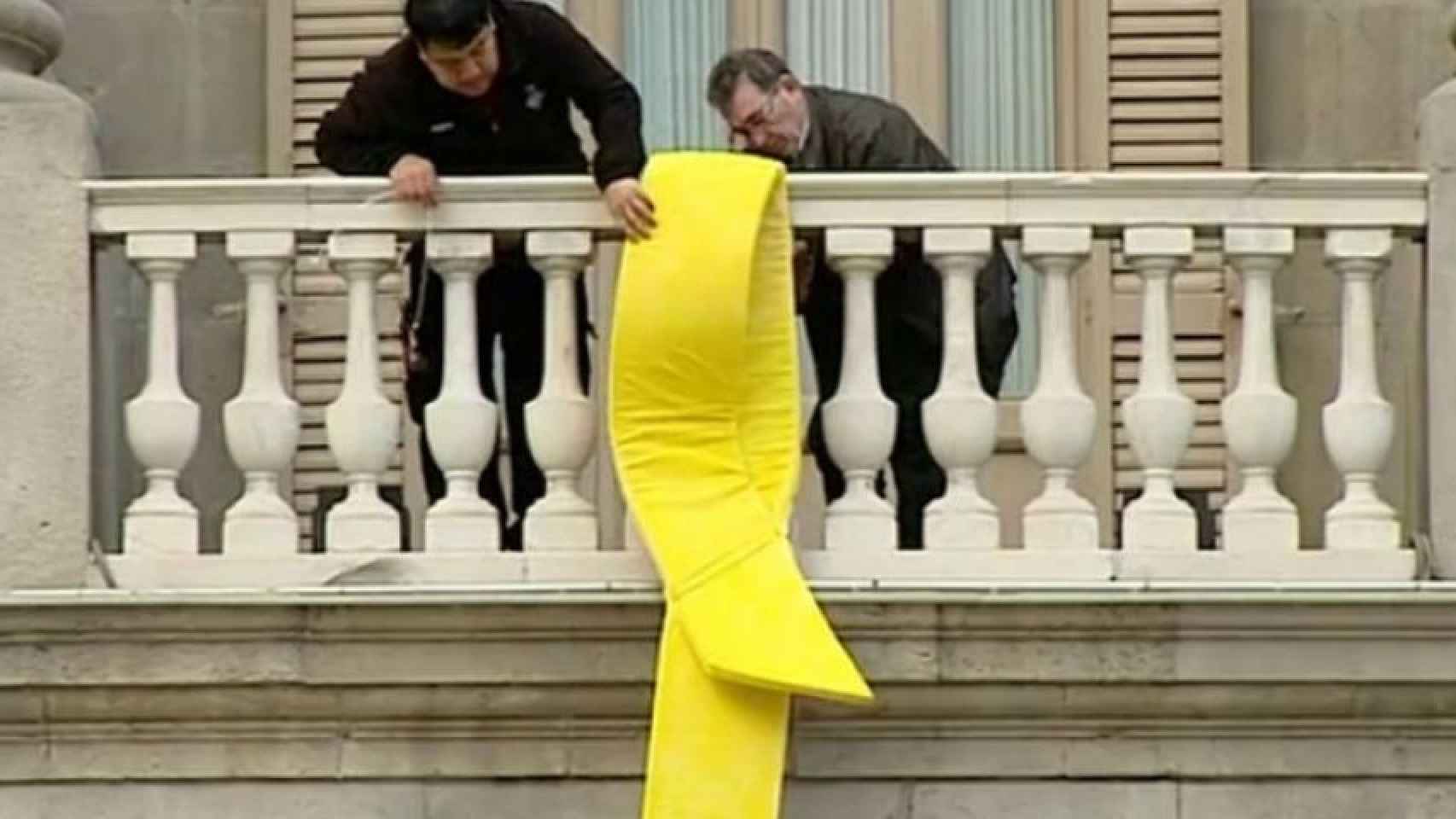 Dos personas en el balcón del Ayuntamiento de Barcelona retirando el lazo amarillo de la fachada del consistorio