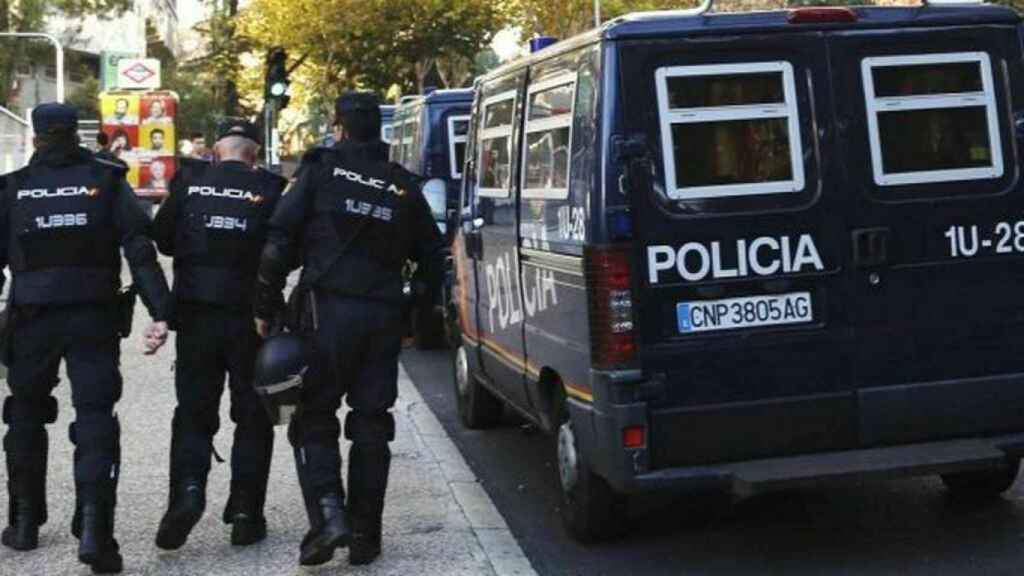 Tres miembros de la Policía Nacional junto a varias furgonetas del cuerpo policial