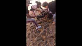 Tres personas ayudan a sacar al hombre, inconsciente, del agua en la playa de la Barceloneta