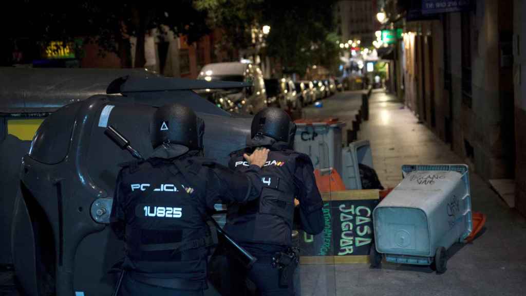 Dos policías junto a varios contenedores tumbados en la vía / EFE