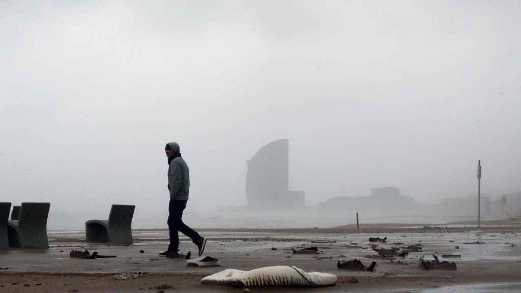 Una persona pasea por la playa con el viento de cara durante el temporal Gloria que ha azotado Barcelona
