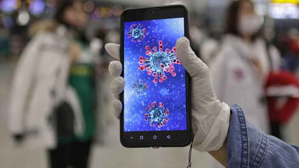 Una persona sujetando un teléfono con la imagen del coronavirus