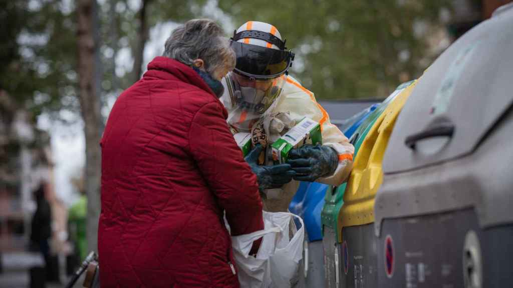 Un trabajador que realiza tareas de desinfección ante el coronavirus  ayuda a una mujer en Barcelona / EUROPA PRESS