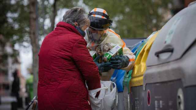 Un trabajador que desinfecta y limpia un contenedor de basura ayuda a una mujer durante la tercera semana de reclusión / EP