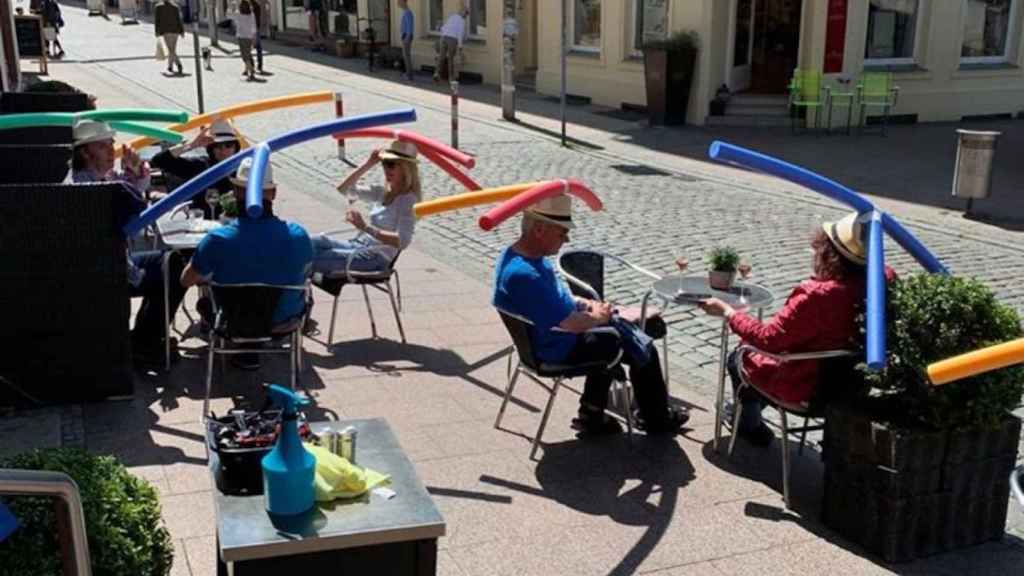 Personas sentadas en una terraza con sombreros con churros de piscina para mantener la distancia de seguridad