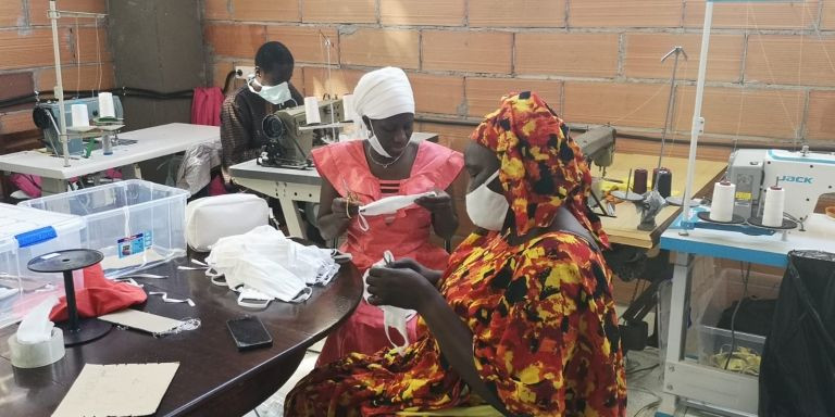 Dos mujeres con vestidos tradicionales africanes confeccionan mascarillas en el taller del sindicato de manteros / G.A