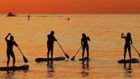 Más personas practicando 'paddle surf' en la playa de la Barceloneta al amanecer