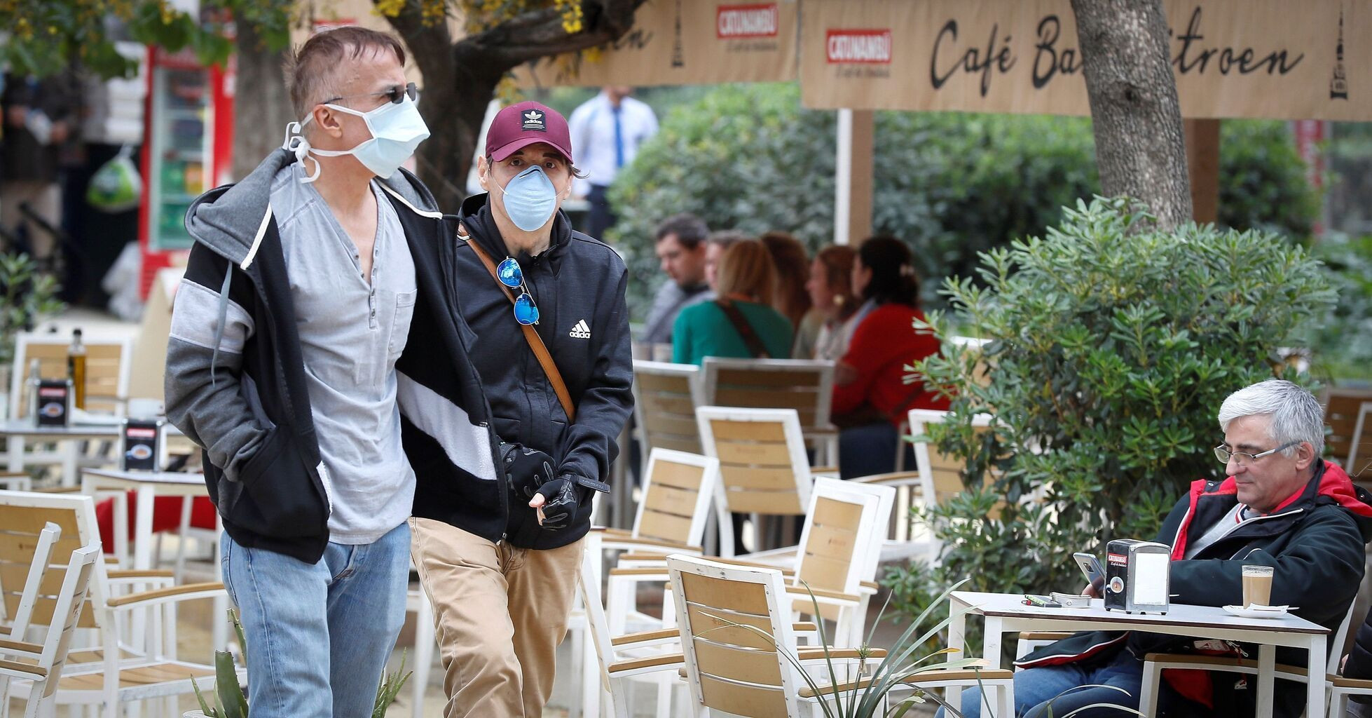 Dos personas con mascarillas caminan junto a la terraza de un bar / EFE