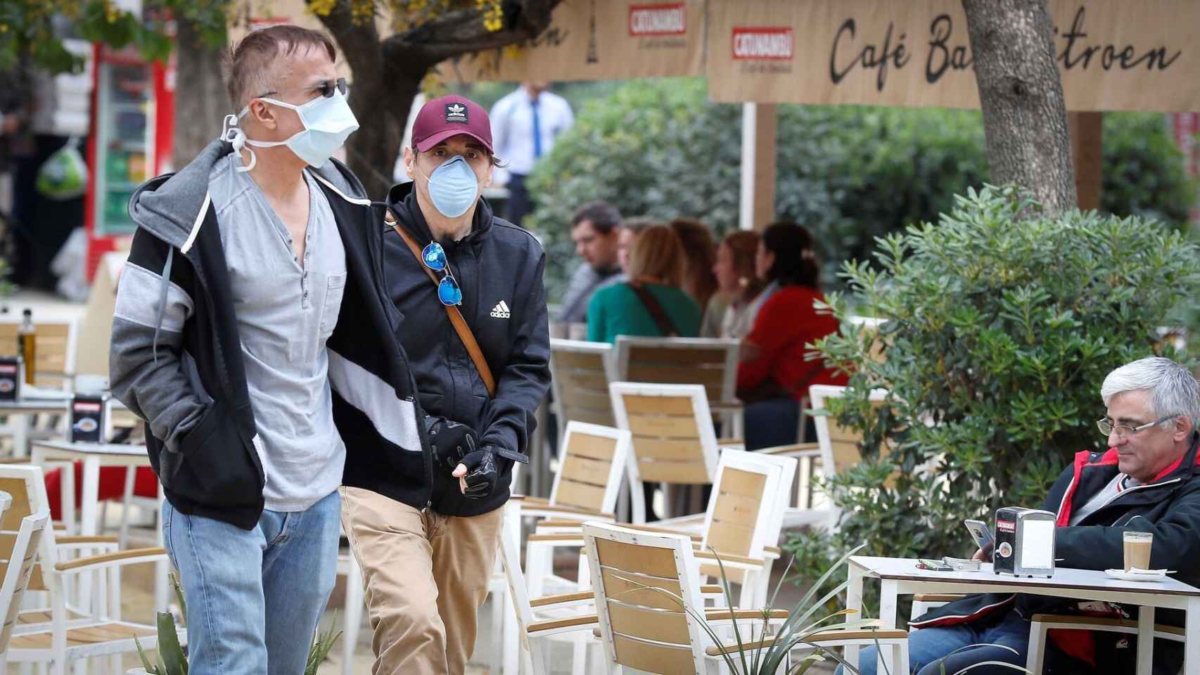 Dos personas con mascarillas caminan junto a la terraza de un bar / EFE