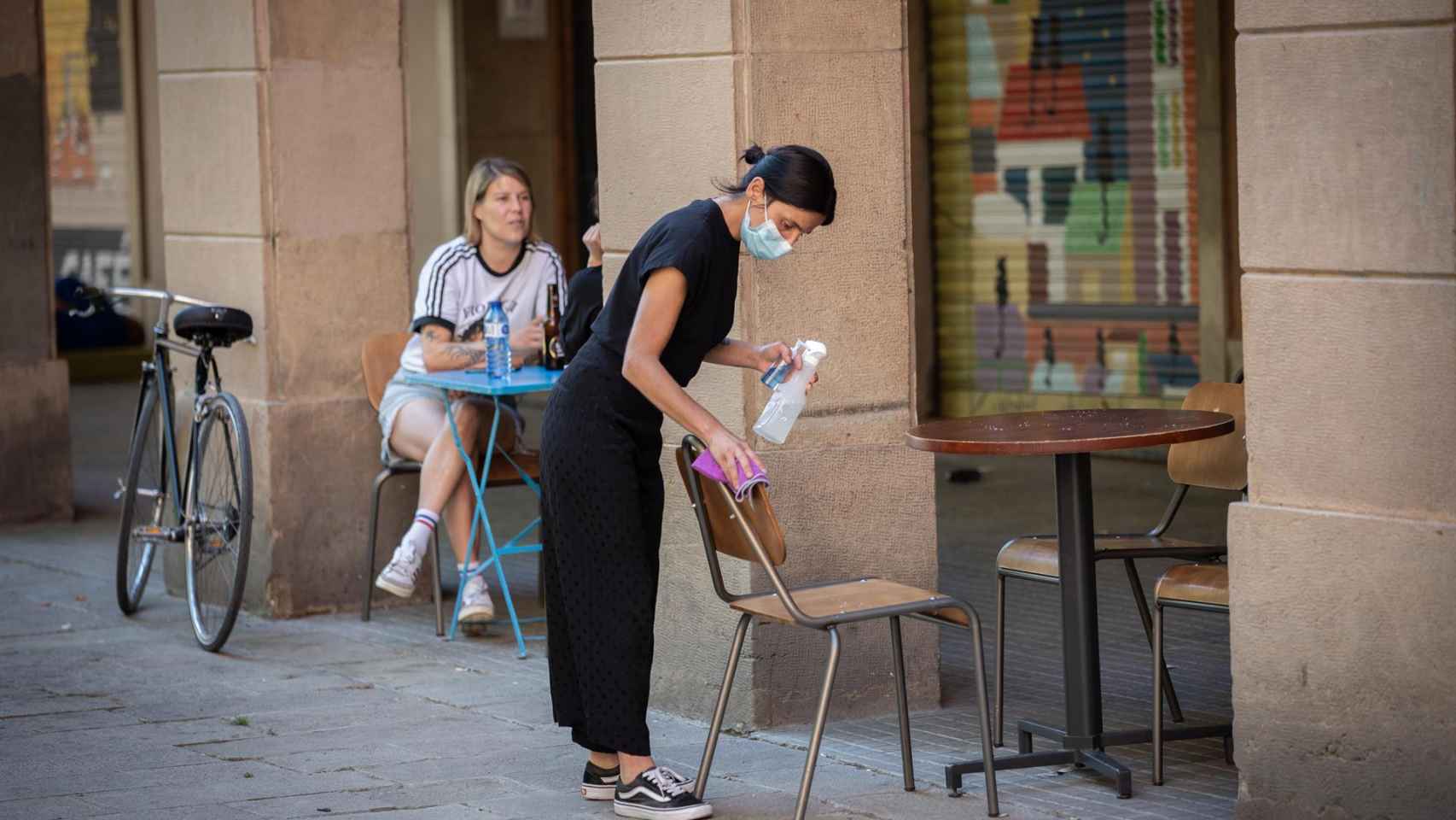 Una camarera limpia varias sillas y una mesa de la terraza de un bar / EUROPA PRESS