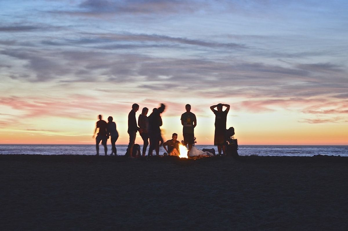 Una decena de personas en la playa con una hoguera encendida