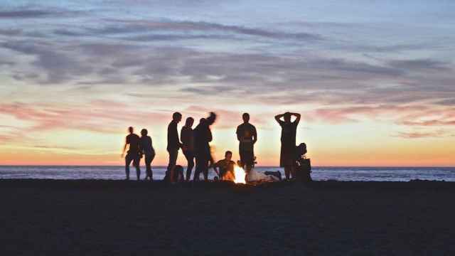 Una decena de personas en la playa con una hoguera encendida