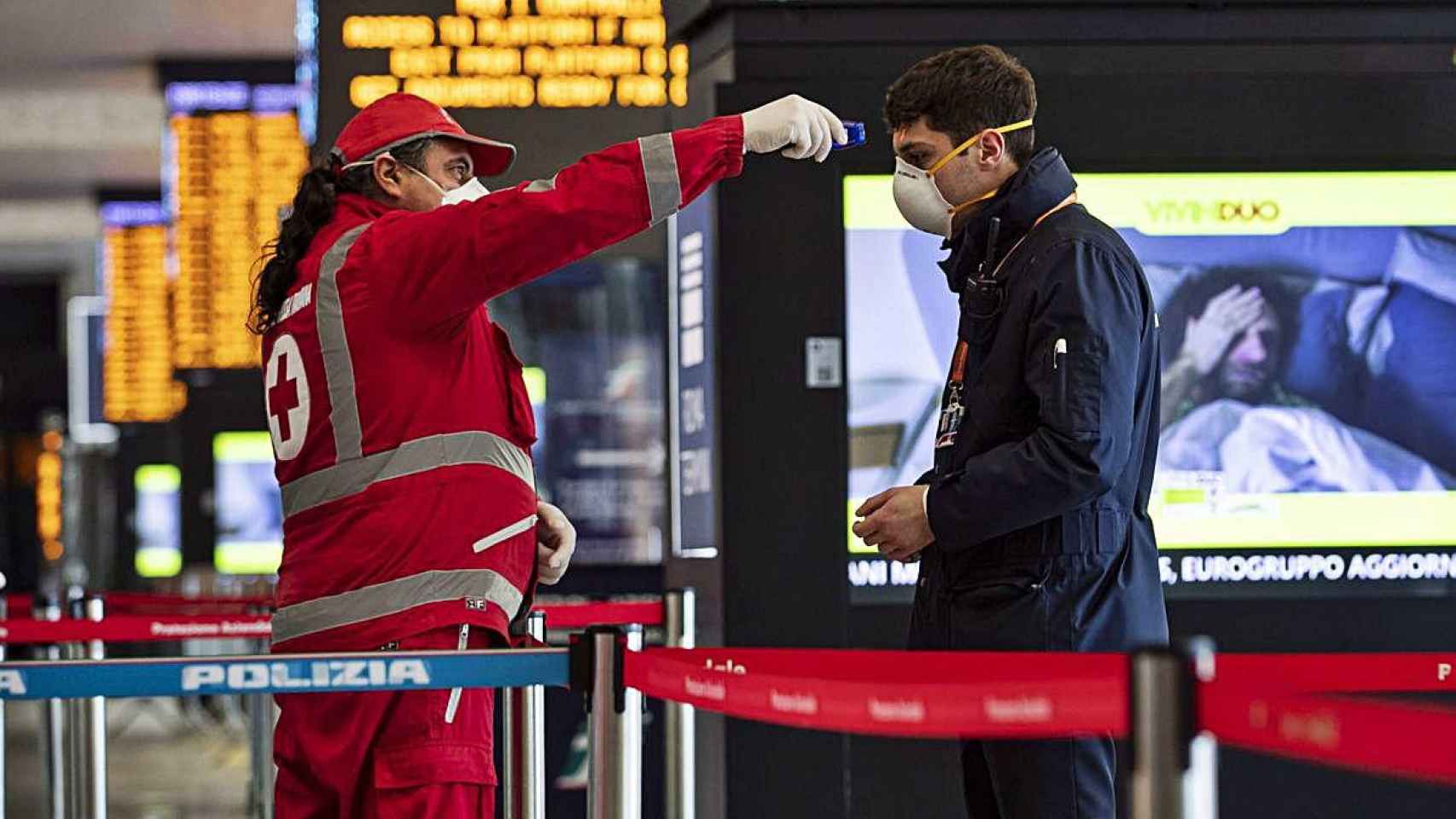 Un profesional tomando la temperatura a un pasajero en una estación de tren