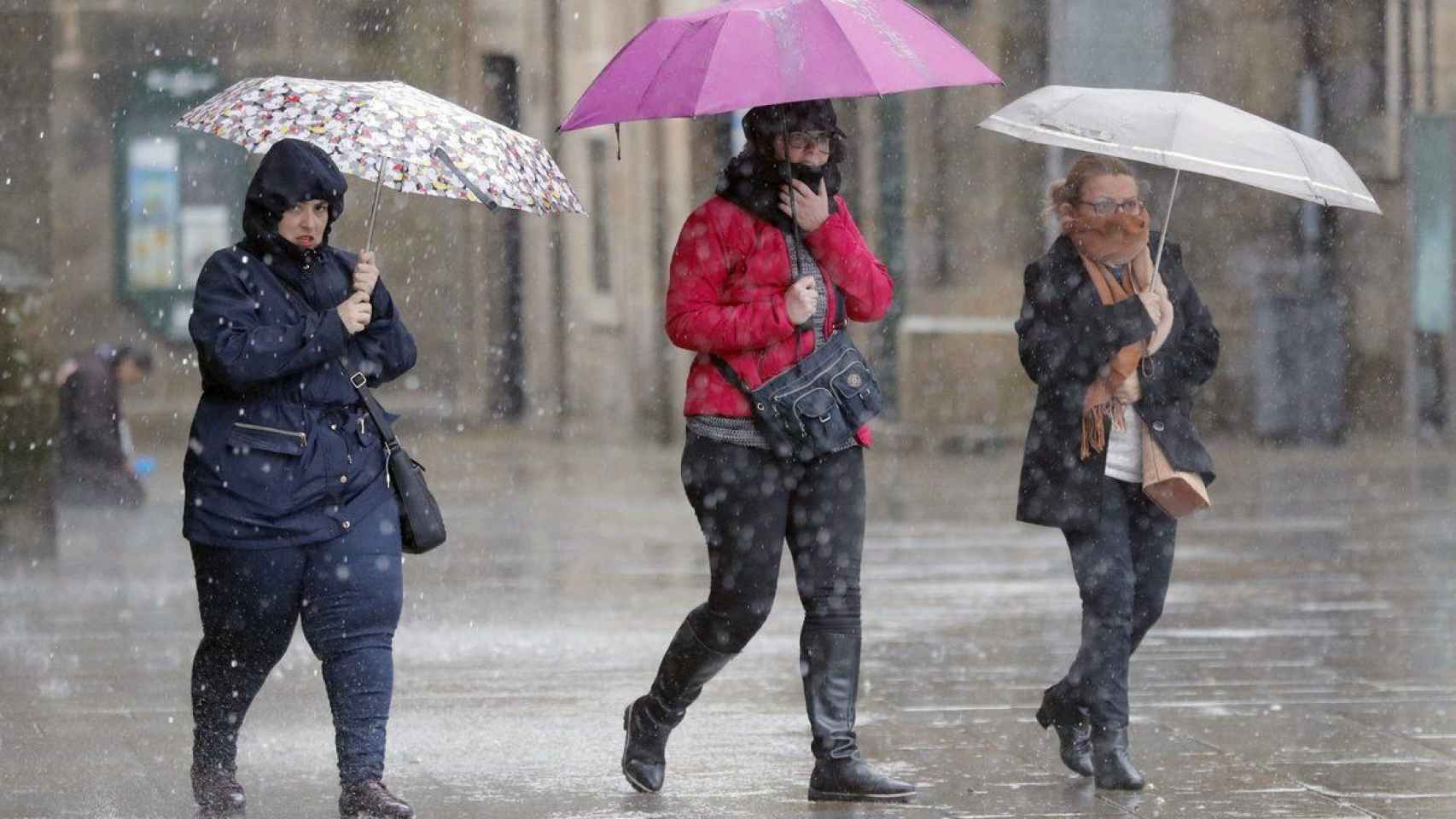 Tres señoras cubiertas con chubasqueros y tapándose de la lluvia / EFE