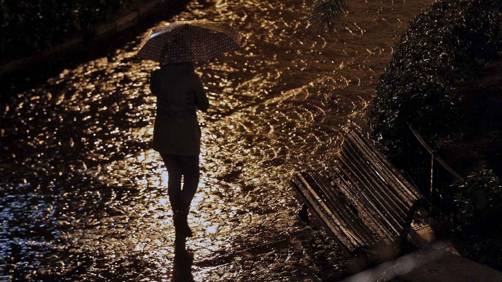 Una mujer camina por la calle en una noche lluviosa / EFE