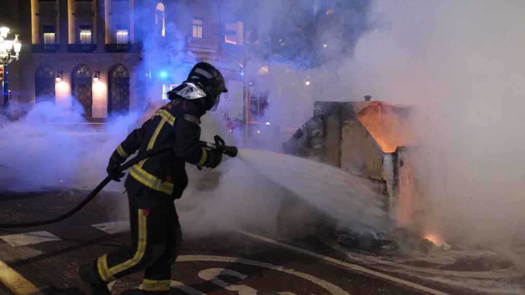 Un contenedor quemado en el centro de Barcelona, apagado por un bombero tras las protestas contra las restricciones / PABLO MIRANZO