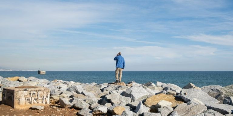 Un hombre habla por el móvil junto al mar, entre la desembocadura del Besòs y las Tres Chimeneas / PABLO MIRANZO