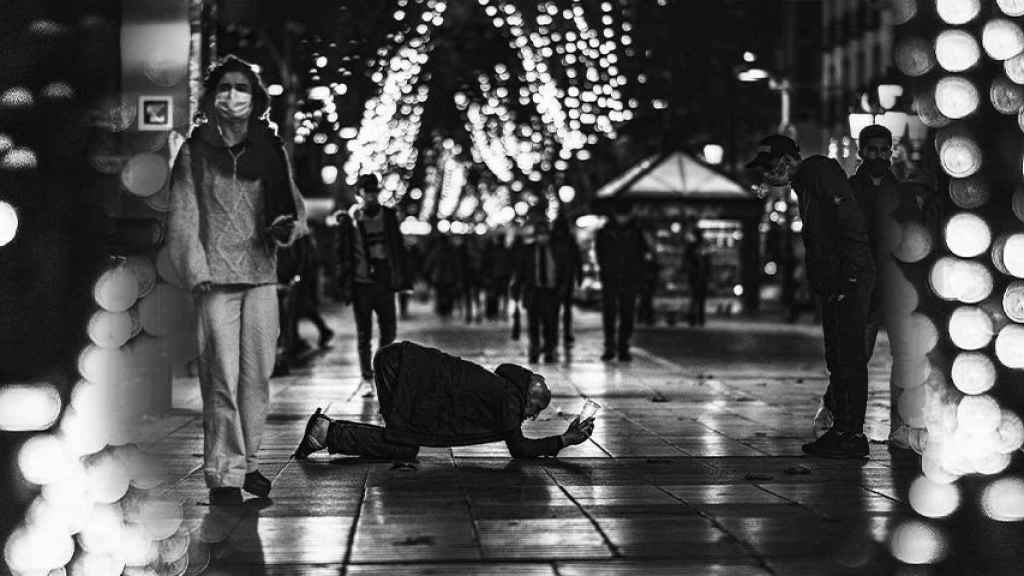 Un hombre pide limosna bajo la atenta mirada de los transeúntes que caminan por La Rambla de Barcelona en 2020 / MARCELO RÍOS - @wolf_rios