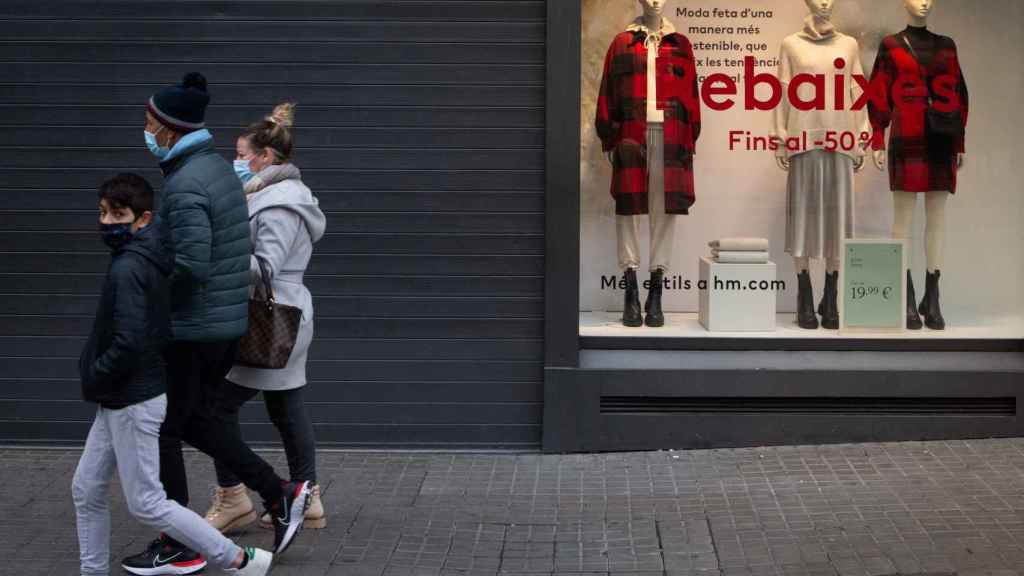 Una familia pasa por delante de una tienda cerrada durante el gélido arranque de las rebajas en Barcelona / EFE