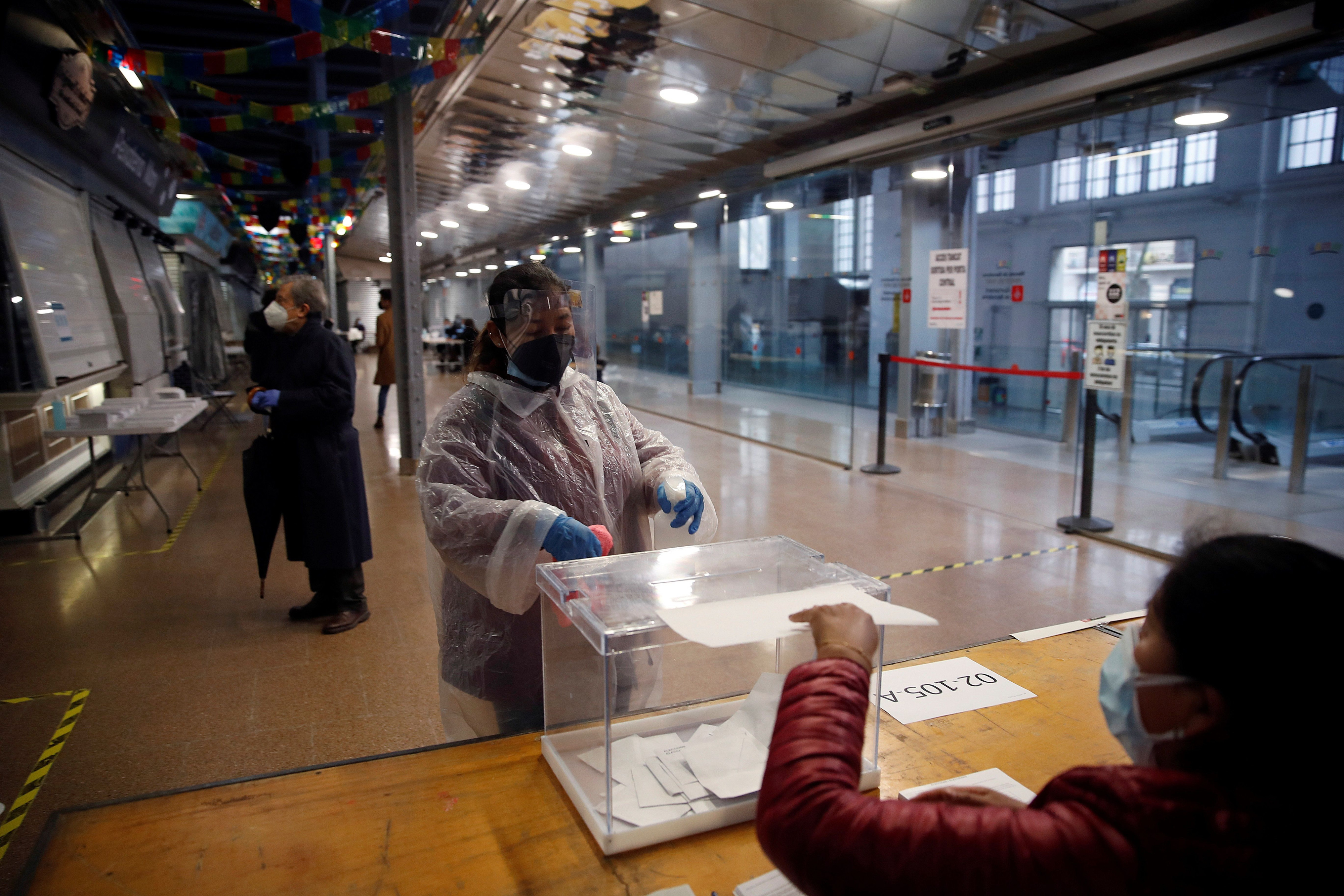 Una mujer protegida con un traje vota en el colegio electoral situado en el Mercat del Ninot en Barcelona este domingo cuando se celebran las elecciones regionales / EFE - Toni Albir