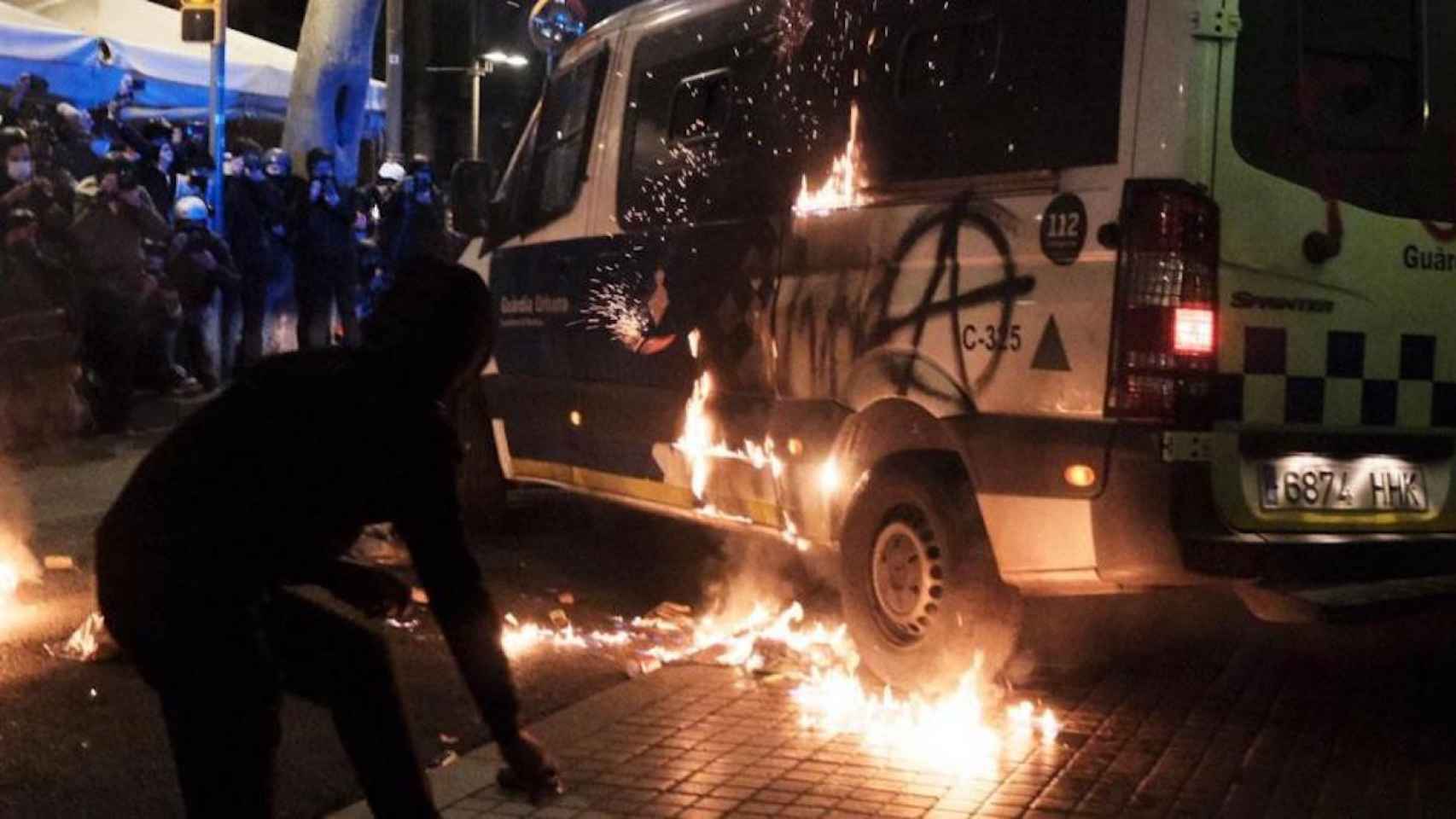 Un radical junto a una furgoneta incendiada de la Guardia Urbana en Barcelona
