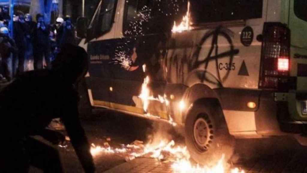 Un joven encapuchado junto a la furgoneta de la Guardia Urbana incendiada / MA - PABLO MIRANZO