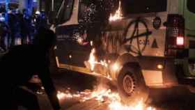 Un joven encapuchado junto a la furgoneta de la Guardia Urbana incendiada / MA - PABLO MIRANZO