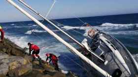 El velero atrapado a las rocas con los efectivos de los Bomberos trabajando para evacuar las personas que estaban adentro