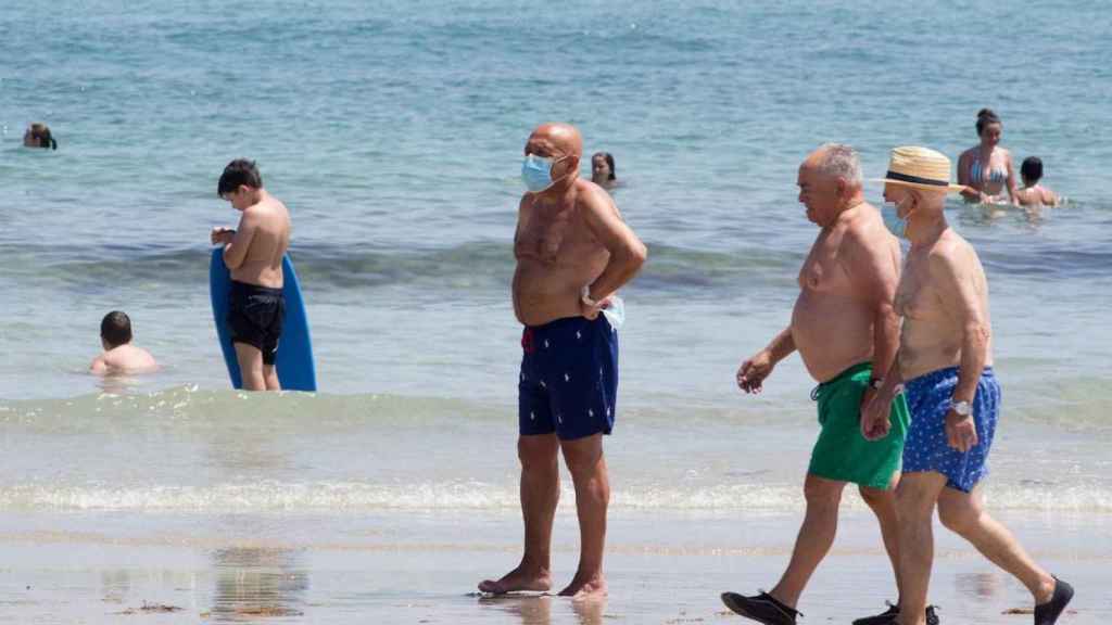 Bañistas y paseantes con y sin mascarilla en una playa / EFE