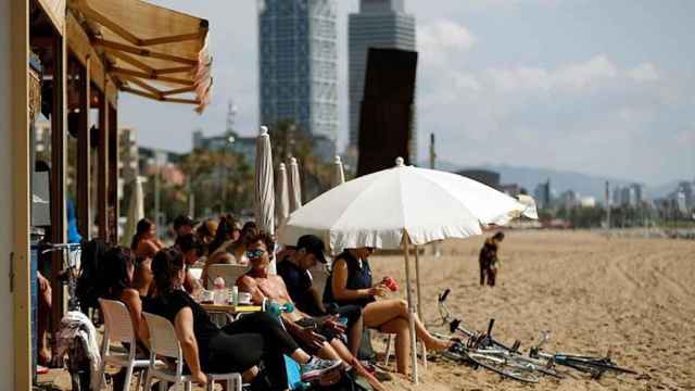 Algunas personas disfrutan de las temperaturas veraniegas en un chiringuito de una playa de Barcelona