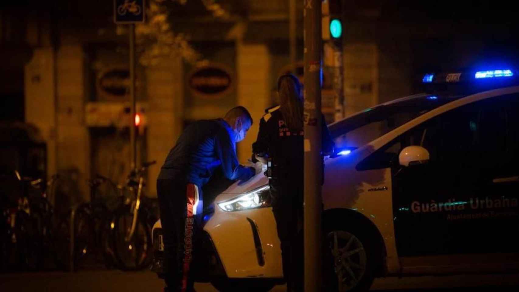 Una agente de la Guardia Urbana con un ciudadano junto a un coche patrulla / EUROPA PRESS