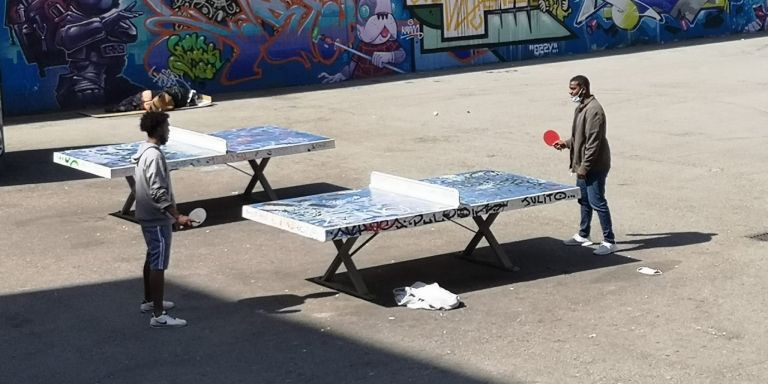 Dos hombres juegan a tenis de mesa mientras un indigente duerme al fondo / GUILLEM ANDRÉS